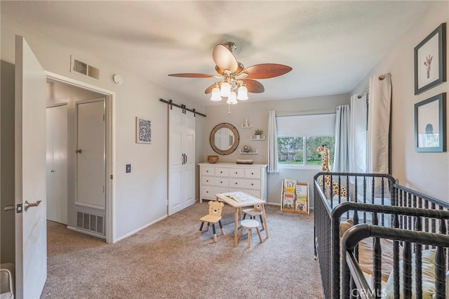 carpeted bedroom with a barn door, a ceiling fan, visible vents, and baseboards