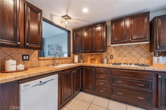 kitchen featuring light tile patterned floors, white appliances, a sink, dark brown cabinets, and tile counters