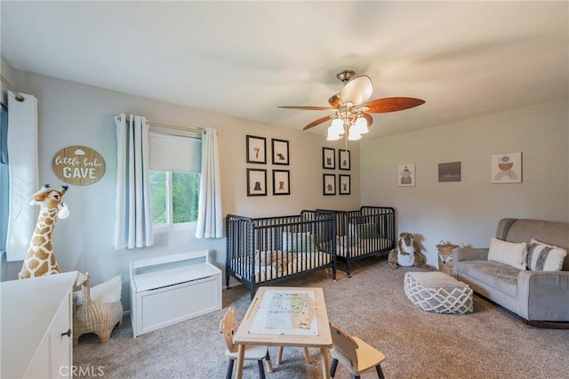 carpeted bedroom featuring a nursery area and ceiling fan