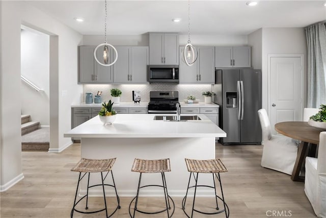 kitchen with gray cabinets, stainless steel appliances, light countertops, a kitchen bar, and a sink