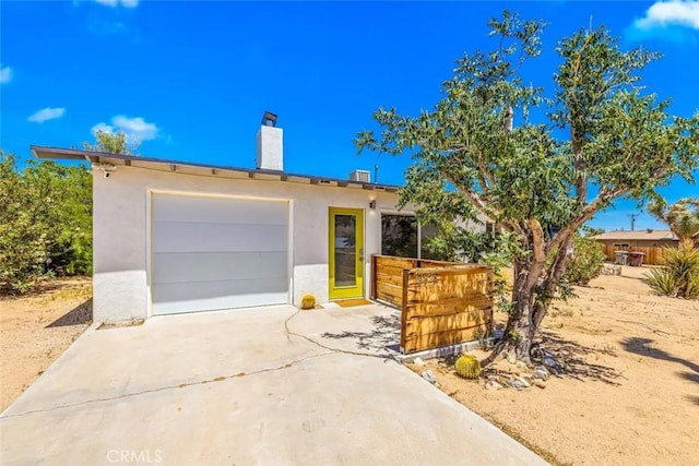 view of front of home with a garage, driveway, a chimney, and stucco siding