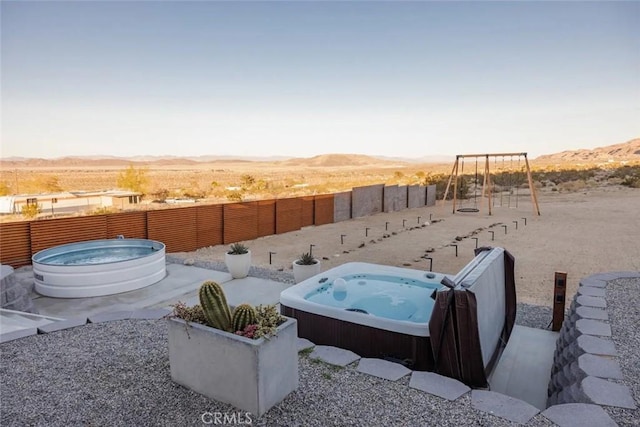 view of yard with a fenced backyard, an outdoor hot tub, a playground, and a mountain view