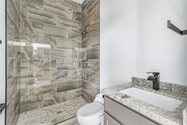 bathroom featuring a tile shower, vanity, and toilet