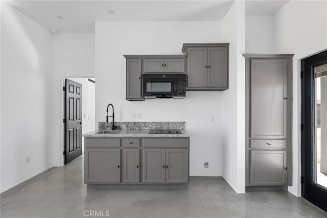 kitchen with a sink, black appliances, gray cabinets, and concrete flooring