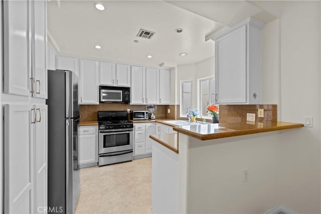 kitchen featuring stainless steel appliances, tasteful backsplash, a peninsula, and white cabinets