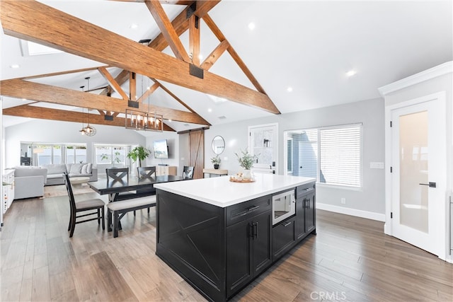 kitchen with open floor plan, wood finished floors, an inviting chandelier, built in microwave, and dark cabinetry