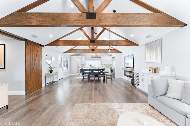 living room featuring light wood-style floors, a barn door, baseboards, and beam ceiling