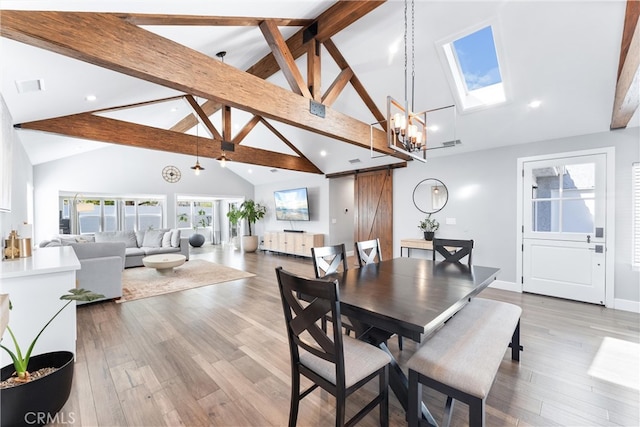 dining room with a skylight, beam ceiling, visible vents, a barn door, and wood finished floors