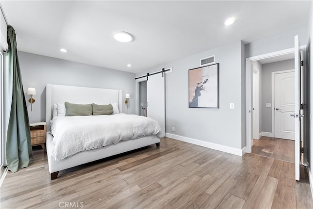 bedroom with light wood finished floors, recessed lighting, visible vents, a barn door, and baseboards