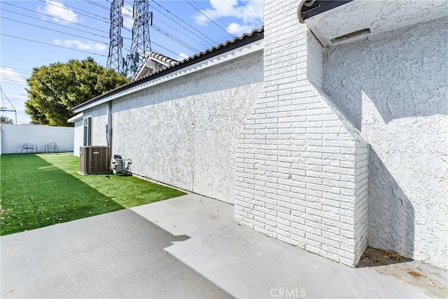 view of side of property with a lawn, a patio, fence, central AC, and stucco siding