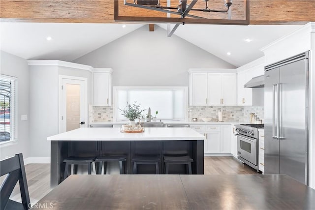 kitchen featuring under cabinet range hood, white cabinetry, a kitchen breakfast bar, high quality appliances, and a center island