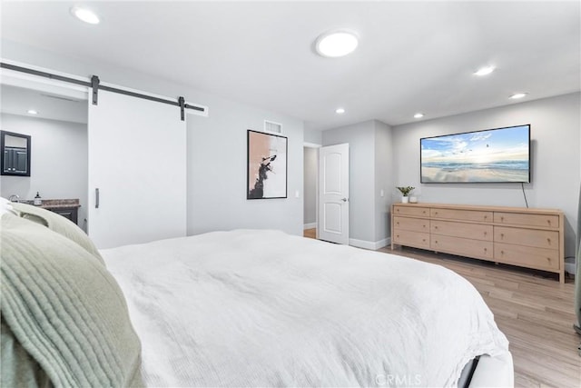 bedroom featuring a barn door, visible vents, baseboards, light wood-style flooring, and recessed lighting