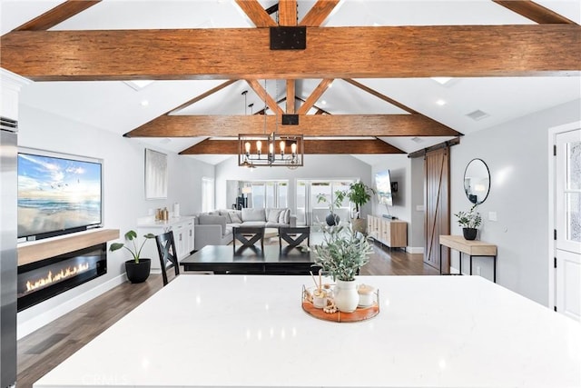 dining space with dark wood-style floors, a notable chandelier, vaulted ceiling with beams, a glass covered fireplace, and baseboards