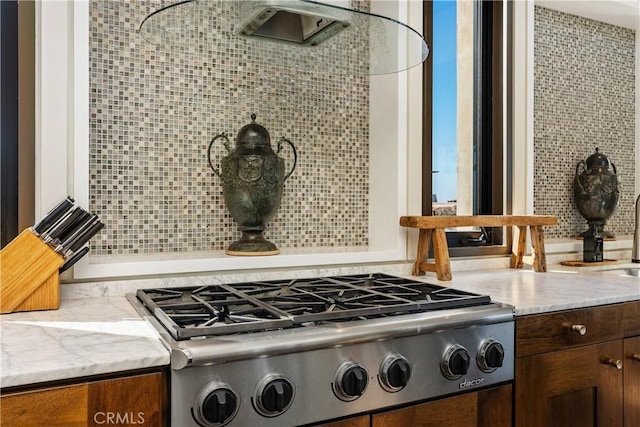 details featuring stainless steel gas stovetop, dark brown cabinets, light stone countertops, and tasteful backsplash