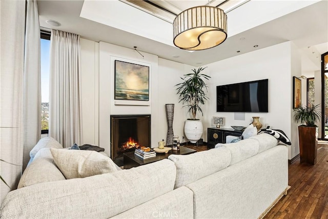 living room featuring dark wood-style flooring and a warm lit fireplace