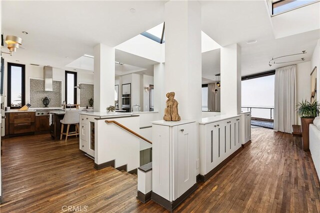 kitchen featuring light countertops, wall chimney range hood, open floor plan, and dark wood-style flooring