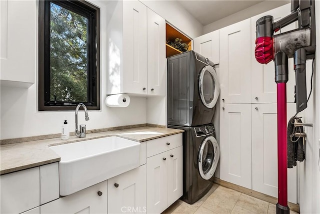 clothes washing area with light tile patterned floors, cabinet space, stacked washer / drying machine, and a sink