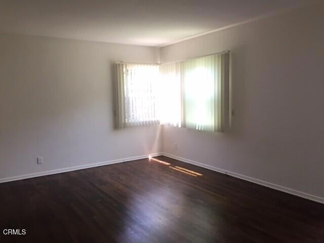spare room featuring dark wood-style flooring and baseboards