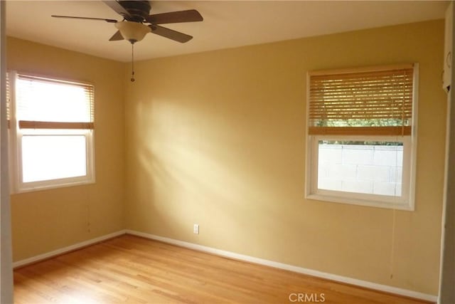 spare room with light wood-type flooring, a ceiling fan, and baseboards