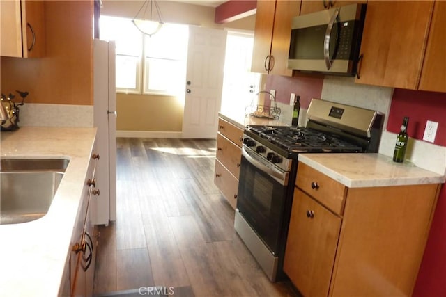 kitchen with brown cabinets, appliances with stainless steel finishes, wood finished floors, and baseboards