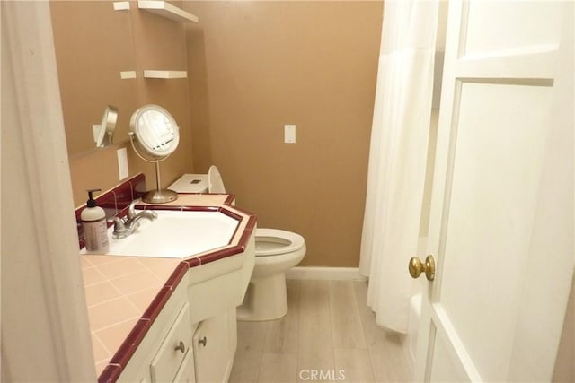 full bath with toilet, baseboards, wood finished floors, and vanity