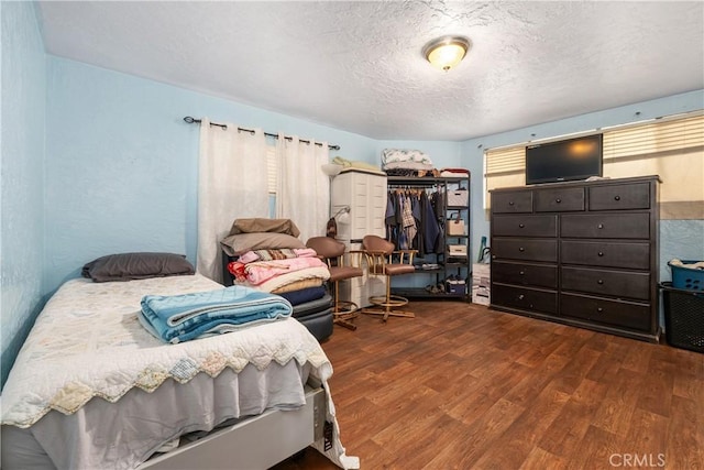 bedroom featuring a textured ceiling, a textured wall, and wood finished floors