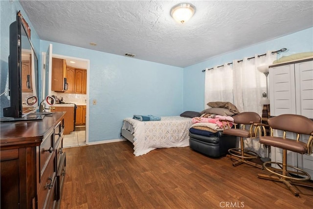 bedroom with visible vents, ensuite bathroom, a textured ceiling, and dark wood-style flooring