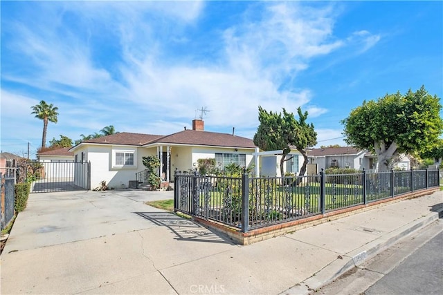 view of front facade featuring a fenced front yard, concrete driveway, a chimney, and stucco siding