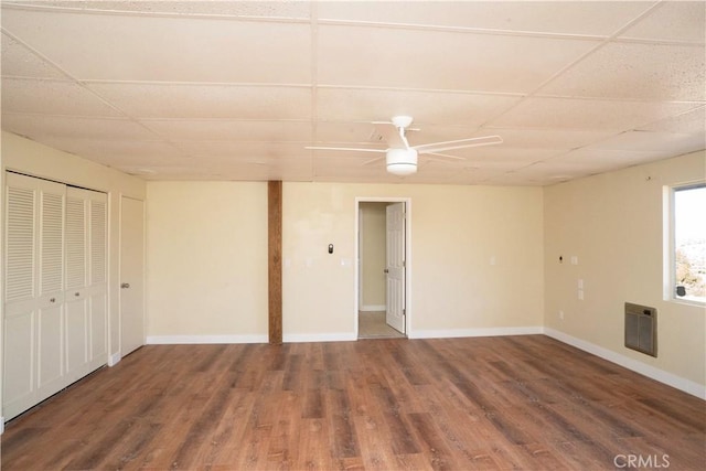 interior space with baseboards, ceiling fan, wood finished floors, heating unit, and a paneled ceiling