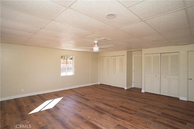 unfurnished bedroom with baseboards, a drop ceiling, wood finished floors, and multiple closets