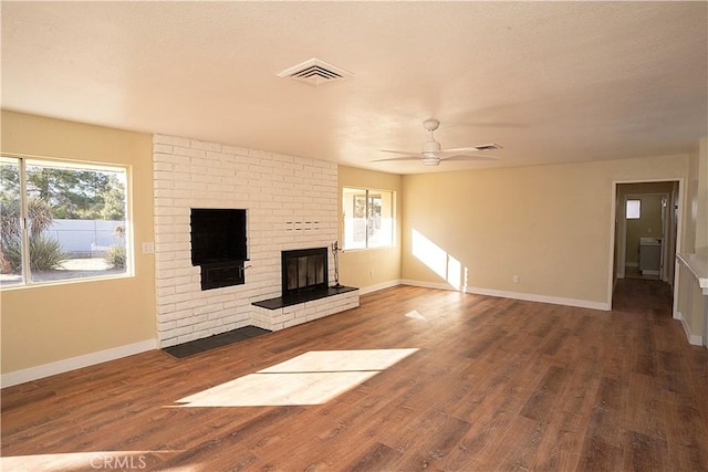 unfurnished living room with a brick fireplace, visible vents, plenty of natural light, and wood finished floors