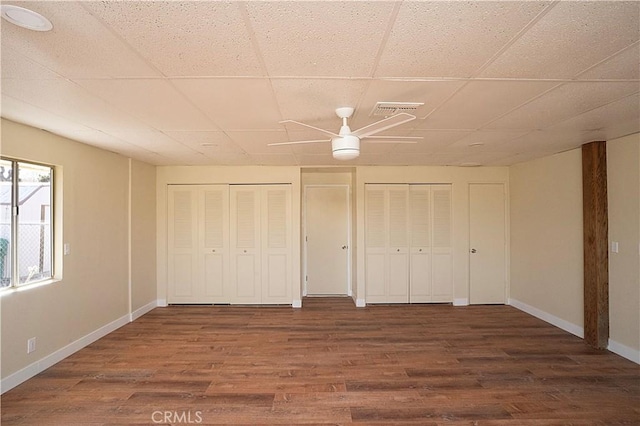 unfurnished bedroom featuring two closets, a paneled ceiling, visible vents, wood finished floors, and baseboards