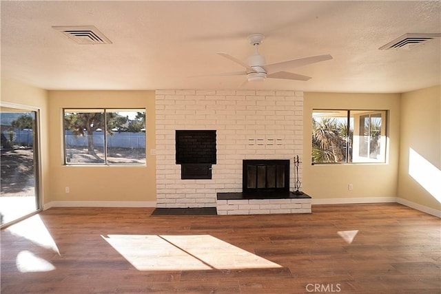 unfurnished living room with a brick fireplace, visible vents, a textured ceiling, and wood finished floors