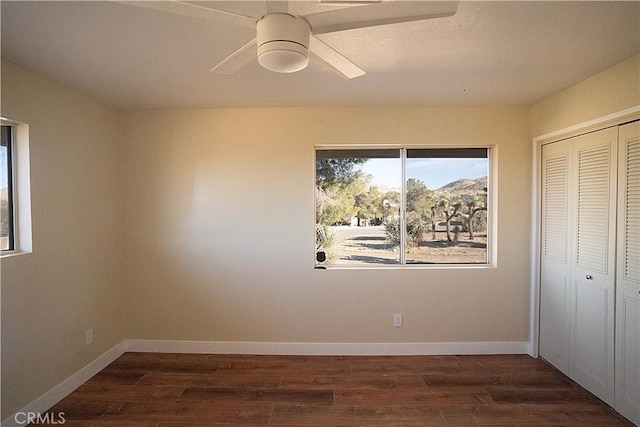 unfurnished bedroom with dark wood-style floors, ceiling fan, a closet, and baseboards