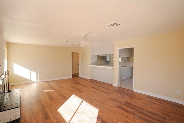 unfurnished living room featuring light wood-type flooring, a fireplace, visible vents, and a ceiling fan