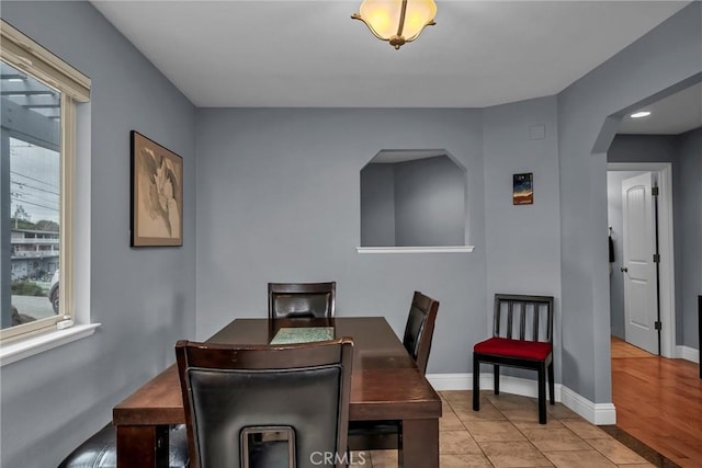 tiled dining area featuring baseboards, arched walkways, and a healthy amount of sunlight