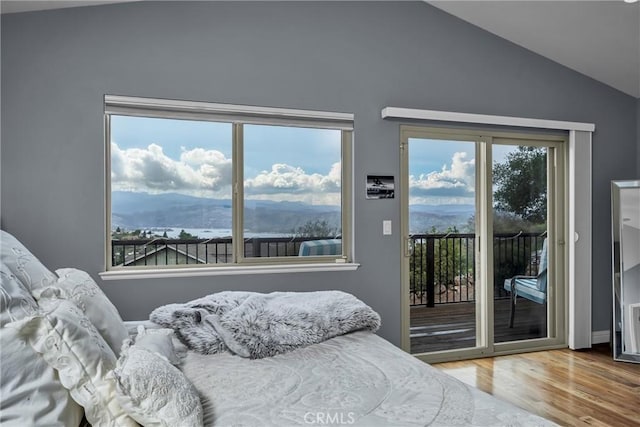 bedroom with access to outside, vaulted ceiling, a mountain view, and wood finished floors