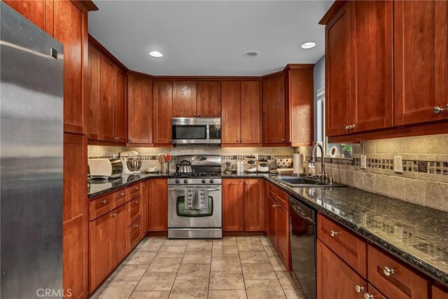 kitchen with stainless steel appliances, a sink, backsplash, and dark stone countertops