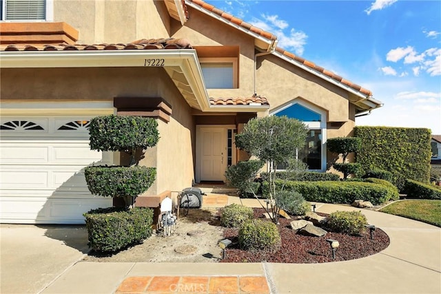 doorway to property featuring an attached garage, a tiled roof, and stucco siding