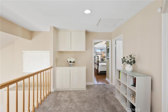 hallway featuring baseboards, attic access, and light colored carpet