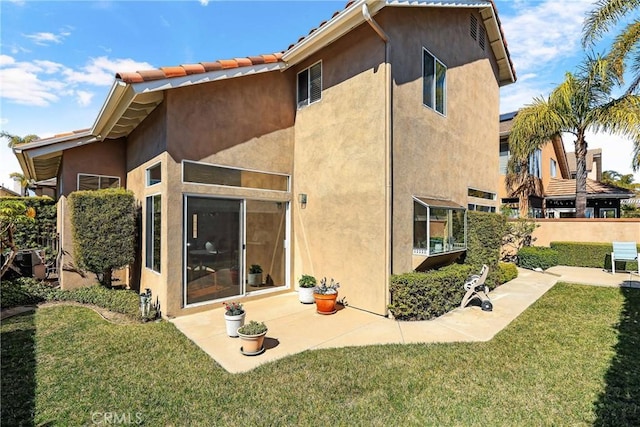 back of property with stucco siding, a lawn, and a patio