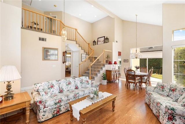 living room with visible vents, an inviting chandelier, wood finished floors, high vaulted ceiling, and stairs