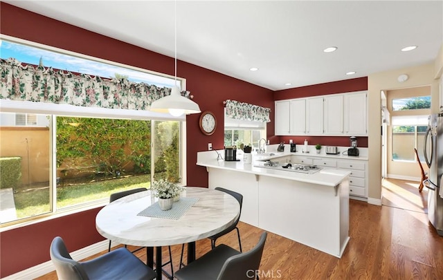 kitchen with white gas stovetop, wood finished floors, a peninsula, light countertops, and white cabinetry