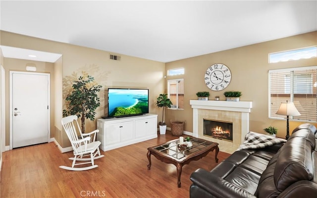 living room with baseboards, a tiled fireplace, visible vents, and wood finished floors