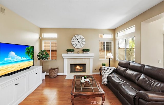 living room featuring visible vents, baseboards, wood finished floors, and a tile fireplace