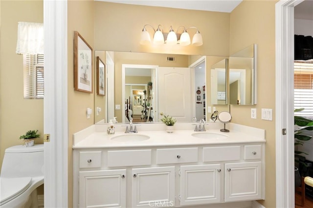 bathroom featuring toilet, double vanity, a sink, and visible vents