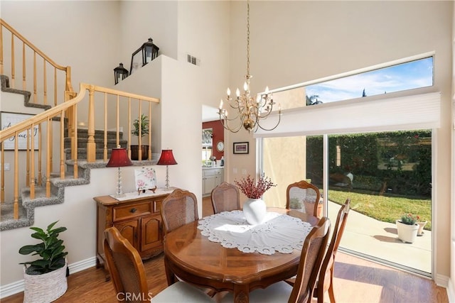 dining space with visible vents, wood finished floors, a high ceiling, stairs, and a chandelier