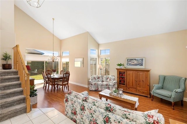 living area with light wood finished floors, baseboards, a chandelier, stairs, and high vaulted ceiling