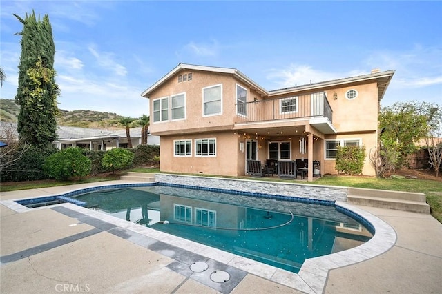 rear view of property featuring a patio area, an outdoor pool, a balcony, and stucco siding