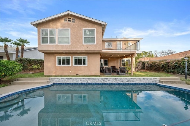 back of house featuring a balcony, a fenced in pool, and stucco siding